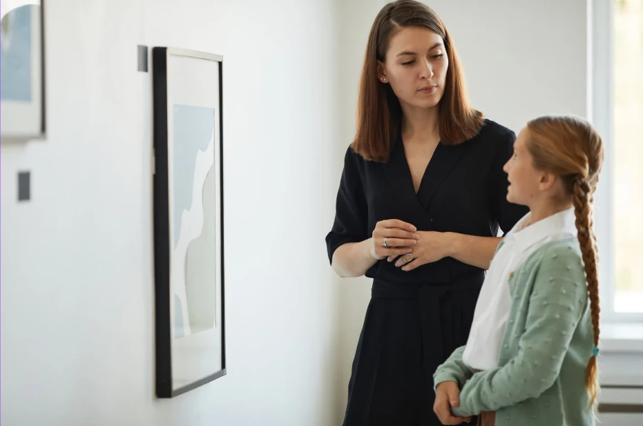A woman and a young girl standing together looking at a framed artwork on a gallery wall