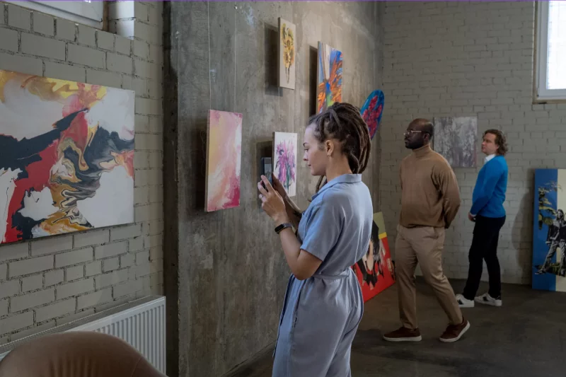 A visitor holding up her phone to a painting hanging in a gallery